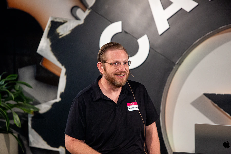 Jonathan Malkin speaking at an event in Austin, wearing a name badge and a lapel microphone.