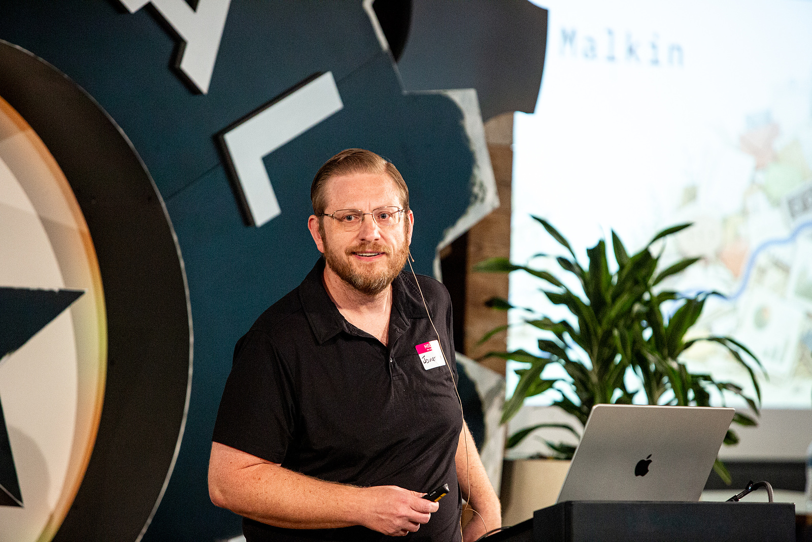 Jonathan Malkin at the Capital Factory podium in Austin, the venue's gear-shaped stage wall behind him.